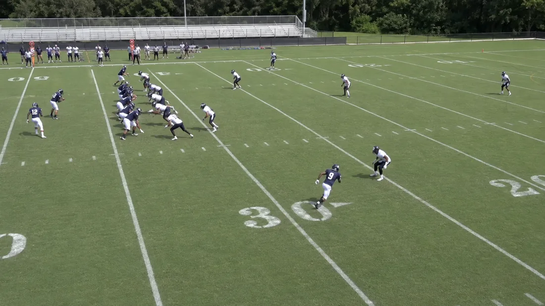 Fictional practice film paused on a navy number nine receiver facing a defender.